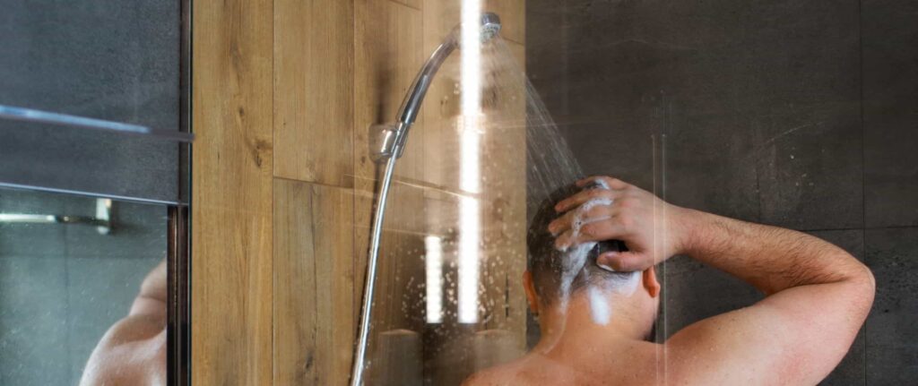 seorang pria mandi dan keramas di bawah guyuran shower