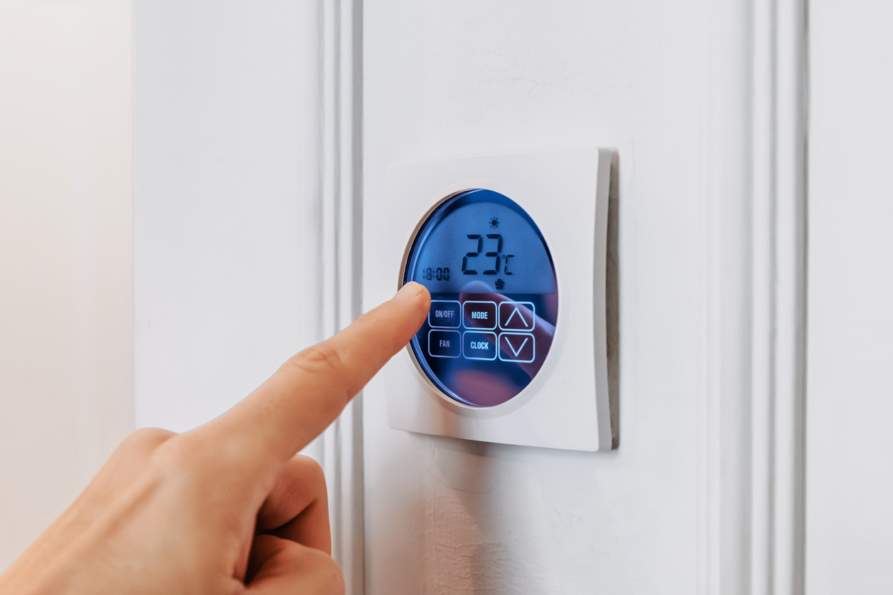 Hand adjusting a modern smart thermostat displaying temperature and settings, managing indoor climate and energy efficiency