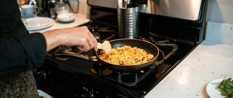 seorang wanita memasak nasi goreng di atas kompor gas