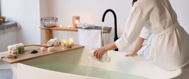 wanita sedang menuangkan garam mandi ke dalam bathtub yang berisi air