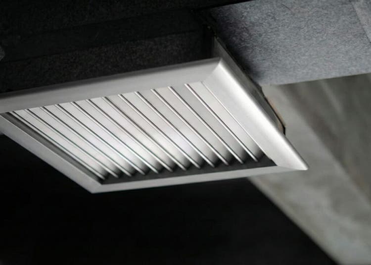 Ventilasi udara logam persegi dengan kisi-kisi terpasang pada langit-langit beton
