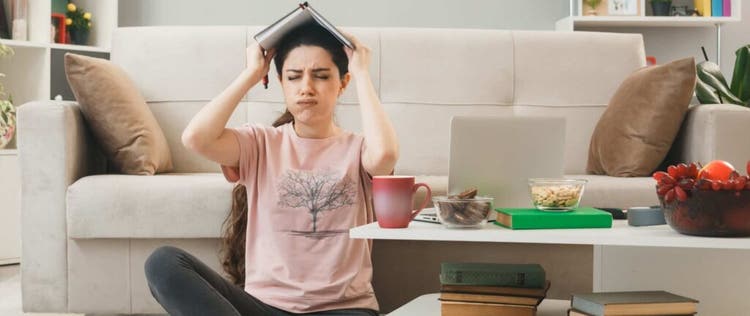 wanita duduk di atas karpet sambil memejamkan mata dan menaruh buku di atas kepalanya