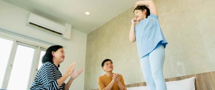 kakek dan nenek bertepuk tangan sambil tersenyum di atas kasur melihat cucu perempuannya